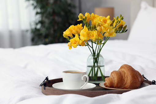 Morning coffee, croissant and flowers on bed indoors