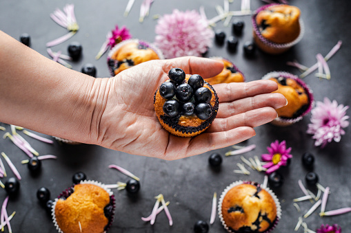 Homemade blueberry muffins  and flowers .
Female hand holding blueberry muffin over floral background.