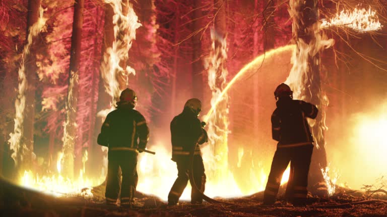 Professional Firefighters Extinguishing Large, High-Priority Part of the Forest Fire. Highly Skilled Hotshot Firemen Crew Working on Challenging Remote Area with Flames Reaching the Treetops