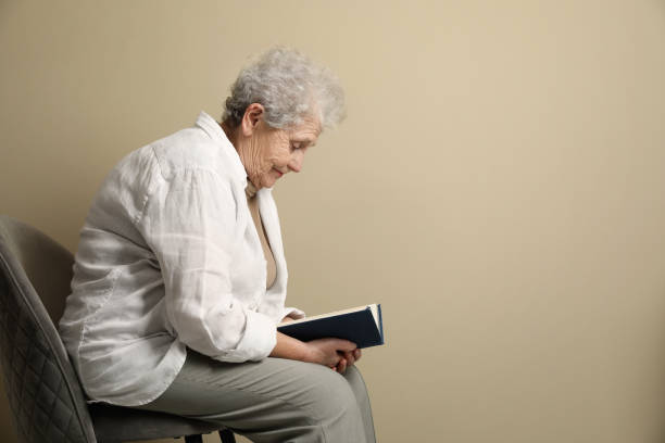 istock Elderly woman with poor posture reading book on beige background. Space for text 1455465646