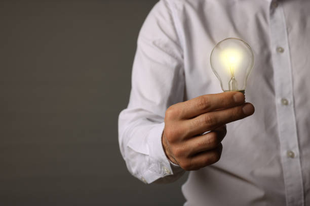 istock Glow up your ideas. Closeup view of man holding light bulb on grey background, space for text 1455465824