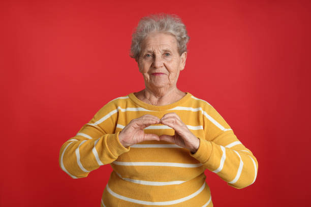 istock Elderly woman making heart with her hands on red background 1455467333