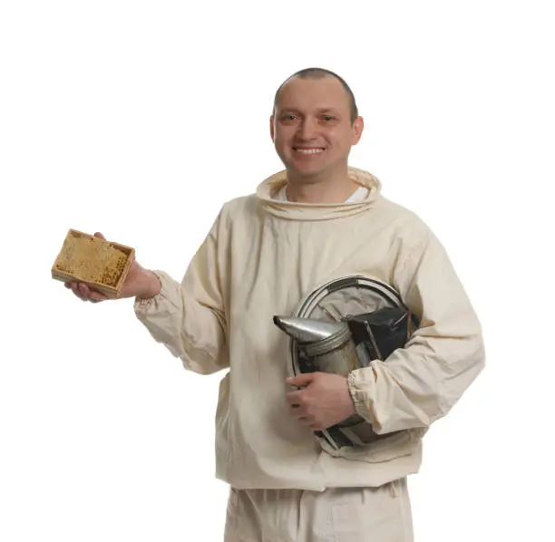 Beekeeper in uniform holding smokepot and hive frame with honeycomb on white background