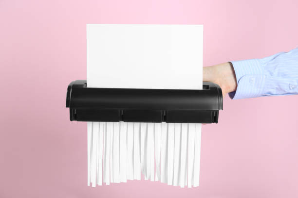 Woman destroying sheet of paper with shredder on pink background, closeup Woman destroying sheet of paper with shredder on pink background, closeup paper shredder stock pictures, royalty-free photos & images