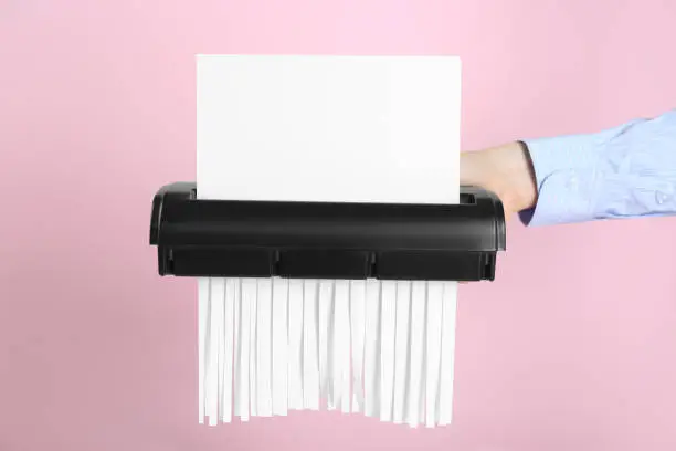 Woman destroying sheet of paper with shredder on pink background, closeup