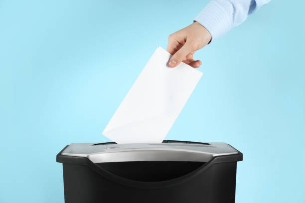 istock Woman destroying envelope with shredder on light blue background, closeup 1455468377