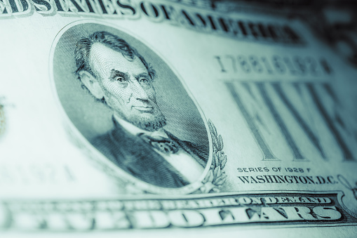 A closeup shot of a portrait of Abraham Lincoln on five US dollar note
