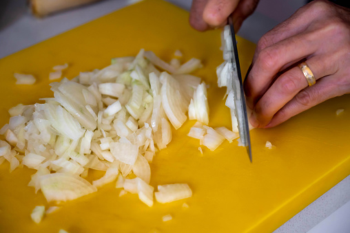 Chopping onion on plastic yellow cutting board.