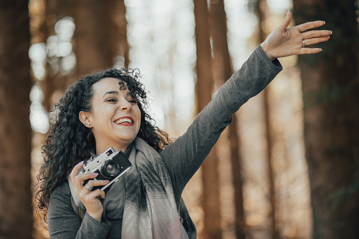 One young woman, a beautiful young woman with curly hair, walking in the forest on a beautiful sunny day, taking photos of the surroundings for her new nature blog