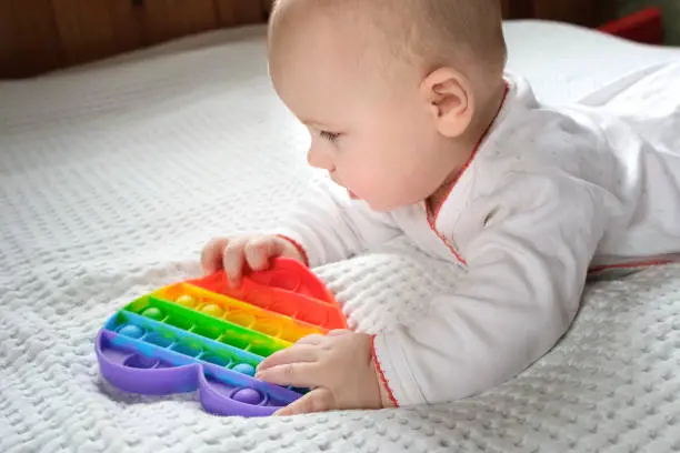 Photo of Happy Kid Playing with Pop It. Newborn Baby Playing with Simple Dimple. The Flexible Sensory Fidget Push-Bubble Toy is Good for Baby Development. Little Child Holds an Eternal Bubble in her Mouth.