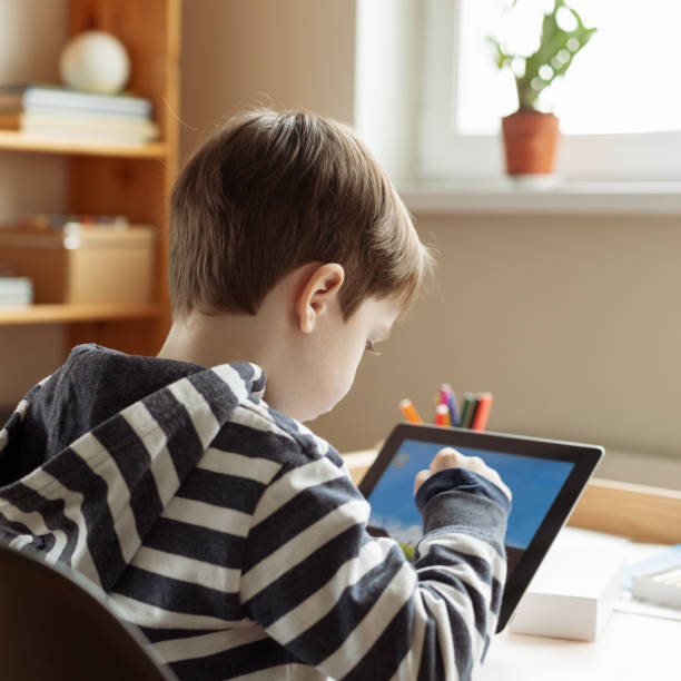 istock White 5 year old boy uses digital tablet while sitting at the table 1455481674