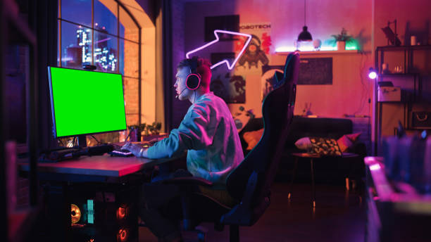 istock Handsome Gamer Playing Online Video Game with a Mock Up Green Screen on His Powerful Personal Computer. Room and PC have Colorful Neon Led Lights. Cozy Evening at Home in Loft Apartment. 1455483838