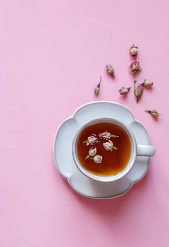 Istanbul, Turkey-January 7, 2023: Black tea in a large white ceramic cup on a pink background. There are pink rose seeds on and around the tea. Shot with Canon EOS R5.
