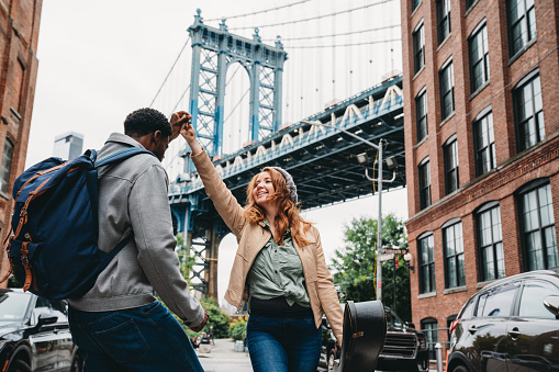 A multi-ethnic couple is dancing in Brooklyn with Manhattan Bridge in the background. They are in Dumbo, a famous district in New York City.