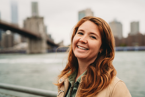 Portrait of a millennial redhead woman in the city. Brooklyn Bridge in the background.