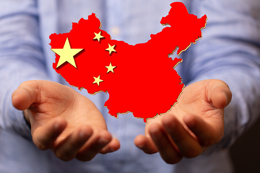 A shallow focus of human hands holding the flag of China in the form of a map