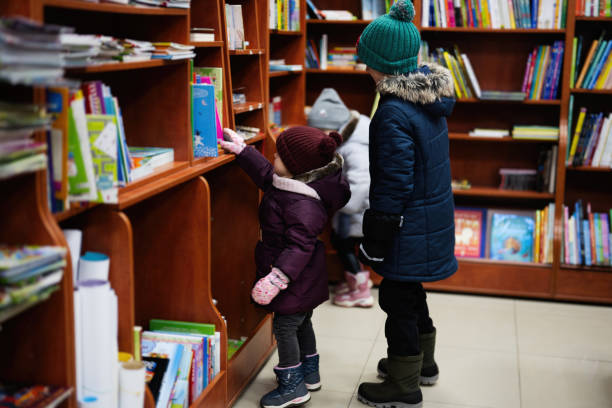 istock Little cute baby in jacket reaching a book from bookshelf at the library. Learning and education of european kids. 1455488077