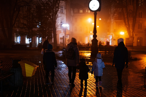 Back of family walking in night city.