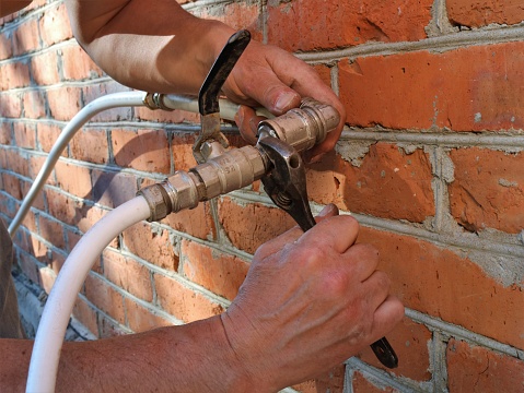 tightening the fastening with a wrench at the junction of metal parts and a plastic pipe when removing water for garden irrigation from the room to the outside and installing a tap