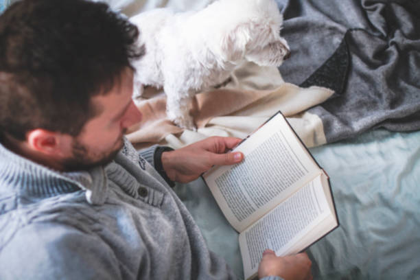istock Man reading book in the bed, cuddling with his dog 1455492126