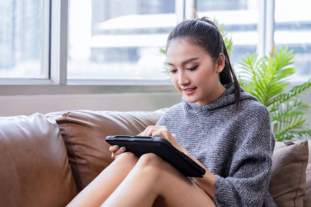 istock young attractive asian female working at home hand use tablet checking search schedule working process planning report with leisure relax on sofa in living room with morning light peaceful moment 1455495973