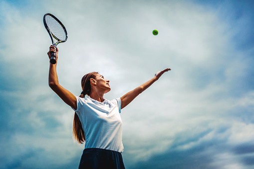 Young handsome female tennis player with racket and ball prepares to serve at beginning of game or match.