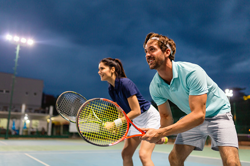Young couple on tennis court. Handsome man and attractive woman are playing tennis. People sport concept
