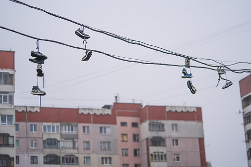many pairs of shoes hang high on the wires between the houses
