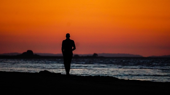 A silhouette of a man walking on the beach at sunset.