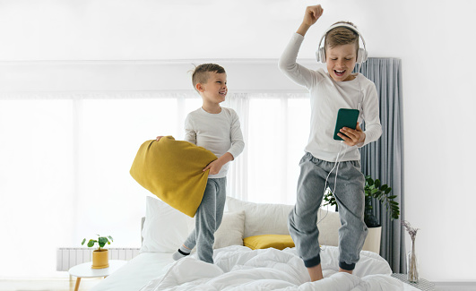 Two brothers jumping on the bed and having fun in the bedroom during morning.
