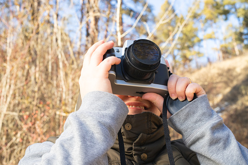 Close up photo of a camera keeping woman in her hands smiling while taking photo being in nature on winter cold sunny day. High quality photo