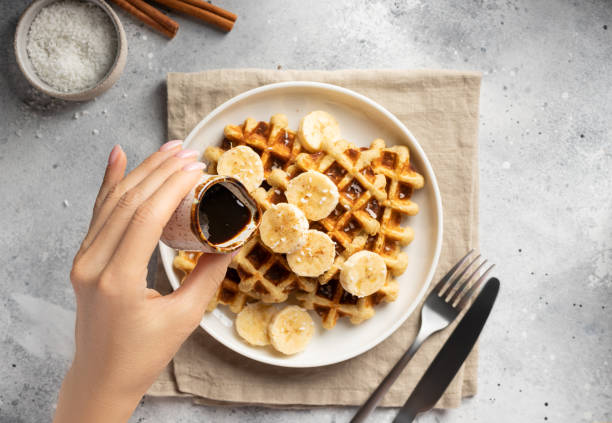 frauenhand gießt dattelsirup auf bananen-haferwaffeln - waffle syrup pouring breakfast stock-fotos und bilder