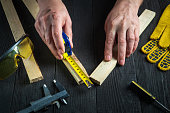 Professional carpenter or woodworker uses a construction tape to measure the length of a piece of wood. Hands of the master close-up at work. Working environment in a carpentry workshop.