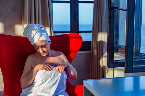 Middle-aged woman after showering sitting in red armchair by window facing the sea on sunny afternoon