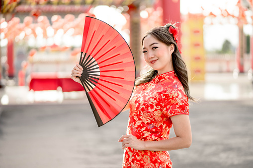 Beautiful Young asian woman wearing traditional cheongsam qipao costume holding fan in Chinese Buddhist temple. Concept of Lunar Chinese new year festival