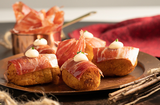 A closeup of Iberian ham croquettes with thin slices on top and kimchi mayonnaise with cilantro.