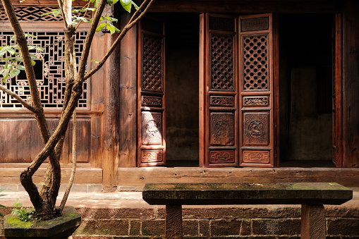 Traditional chinese courtyard house in Yunnan province. Ancient village house garden with trees and plants. Chinese wooden screens texture on the facade in courtyard with stone bench and plants.
