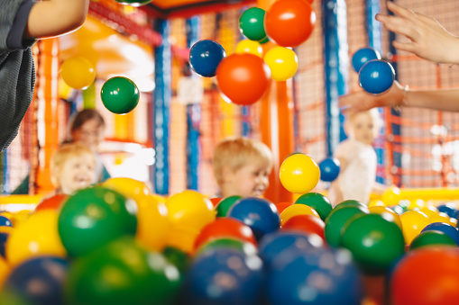 School children having fun in indoor park playground. Happy boy playing at balls pool playground. Boys and girls playing with multi colored plastic balls in big dry paddling pool in playing centre