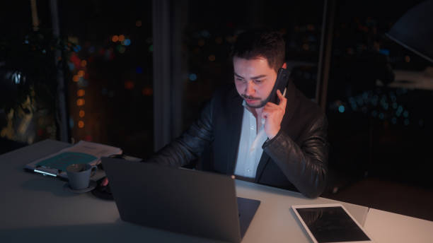 istock Young businessman working late at office and talking on phone at night 1455519366