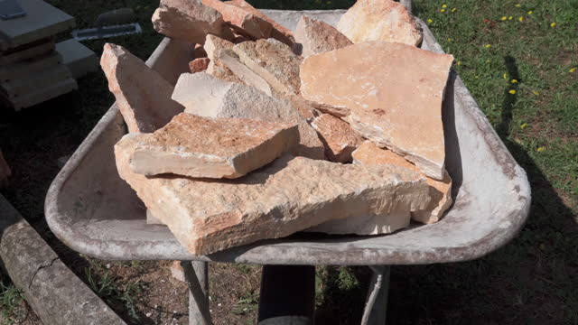 Orange rock stones of different shapes in wheelbarrow, preparation of industrial material on construction site for installation on the wall, house improvement concept