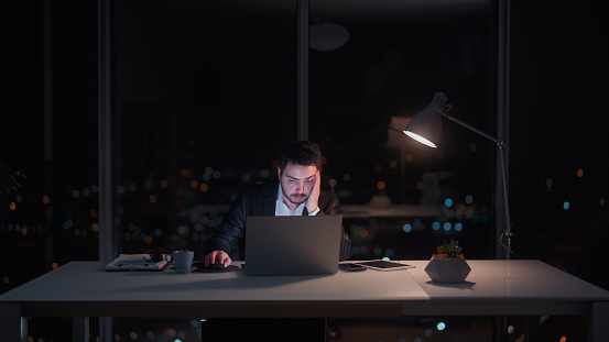 A young businessman is working late at an office at night.