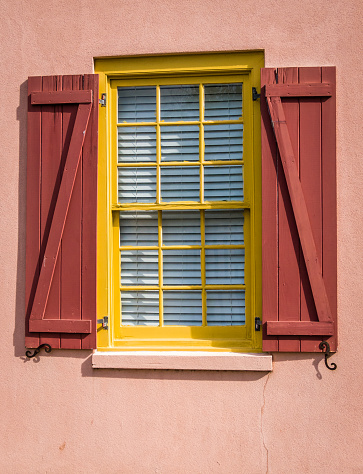 A yellow window on a pink stucco wall with red shutters on a building in St. Augustine, Florida.