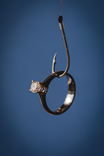 Solitaire diamond ring hanging at fishing hook . Representing online dating apps and phishing concepts.