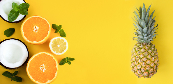 Pineapple, orange, lemon and coconut on the yellow background. Banner. Copy space. Top view. Close-up.