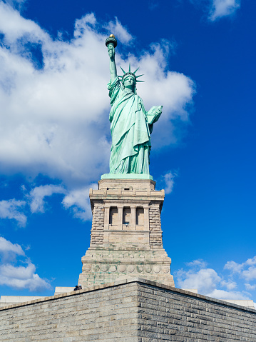A low angle vertical view of the Statue of Liberty National Monument under blue sky in New York