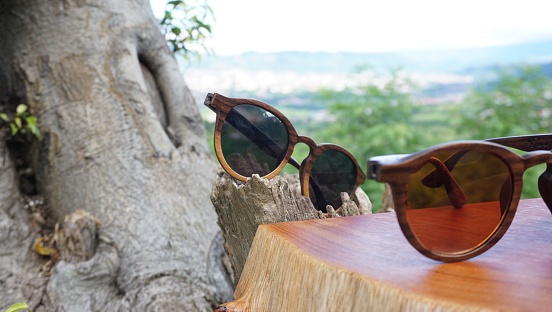 Two sunglasses left on a wooden surface against a blurred background