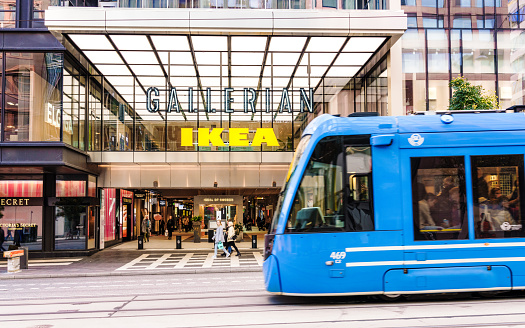 Stockholm, Sweden - A full tram passing pedestrians near the entrance to the Gallerian shopping mall in Stockholm's city centre, with a sign for Ikea among other brands.