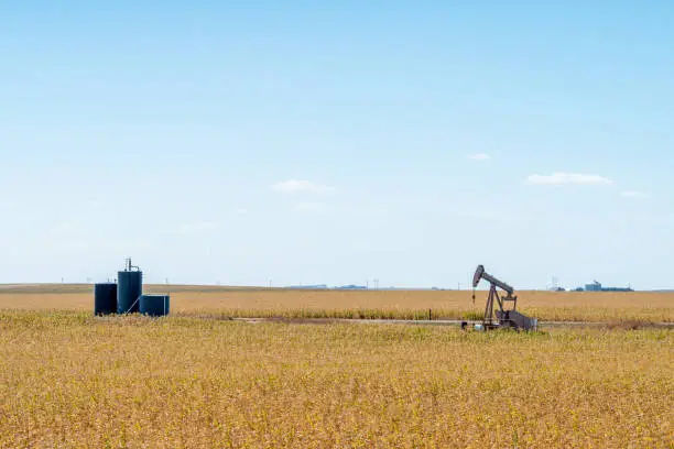 Photo of Wide Angle Shot of an Oil Pump Jack and Storage Tanks in Kansas with a Beautiful Autumn Blue Sky Background