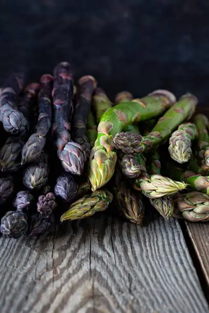 Raw purple, green asparagus on a dark wooden background. Raw food concept, place for copy space.
