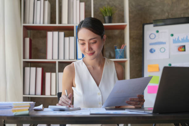 istock Asian Businesswoman Using laptop computer and working at office with calculator document on desk, doing planning analyzing the financial report, business plan investment, finance analysis concept. 1455534451